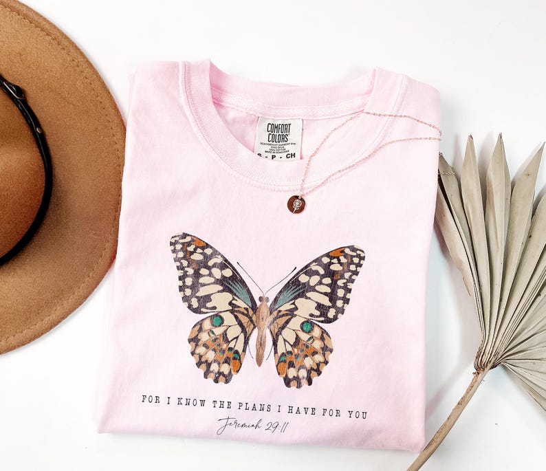 May include: Pink t-shirt with a butterfly graphic and the text "For I know the plans I have for you Jeremiah 29:11".