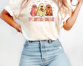 May include: A cream-colored short-sleeve t-shirt featuring a graphic of three ghosts in pink, yellow, and orange, each holding a different food item. Above the ghosts are small bats and spiderwebs. The text PANTASMAS is printed in pink and orange.