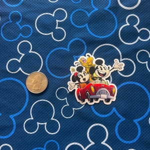 May include: A sticker featuring Mickey Mouse, Minnie Mouse, and Pluto driving a red car on a blue background with white Mickey Mouse outlines.