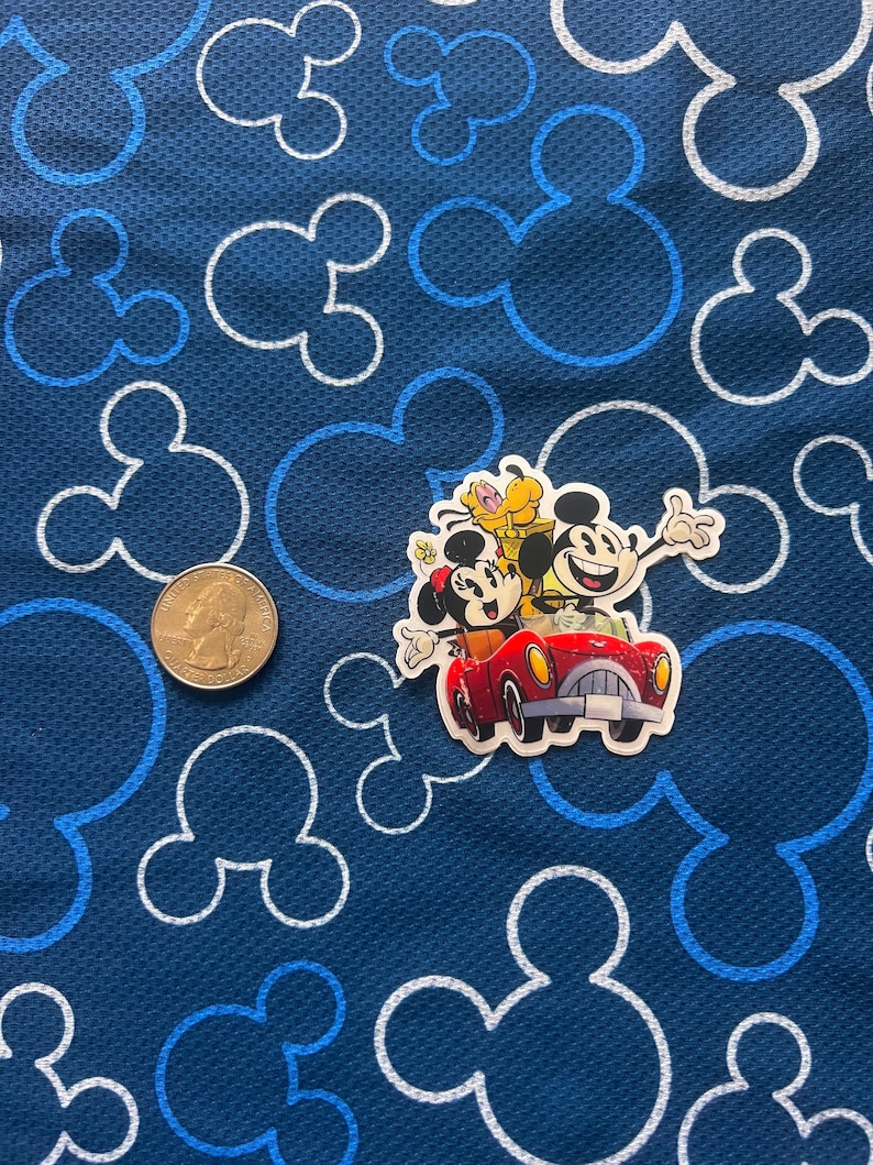 May include: A sticker featuring Mickey Mouse, Minnie Mouse, and Pluto driving a red car on a blue background with white Mickey Mouse outlines.