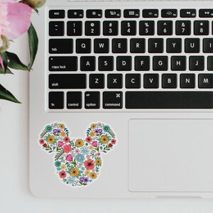 May include: A floral Mickey Mouse design sticker on a laptop. The sticker is made up of colorful flowers and leaves.
