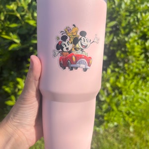 May include: A pink stainless steel tumbler with a Mickey Mouse, Minnie Mouse, and Pluto sticker. The sticker shows the characters riding in a red car.