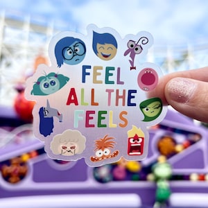 May include: A clear sticker with the text "Feel All The Feels" in rainbow colors. The sticker features characters from the movie Inside Out, including Joy, Sadness, Fear, Anger, Disgust, and Bing Bong.