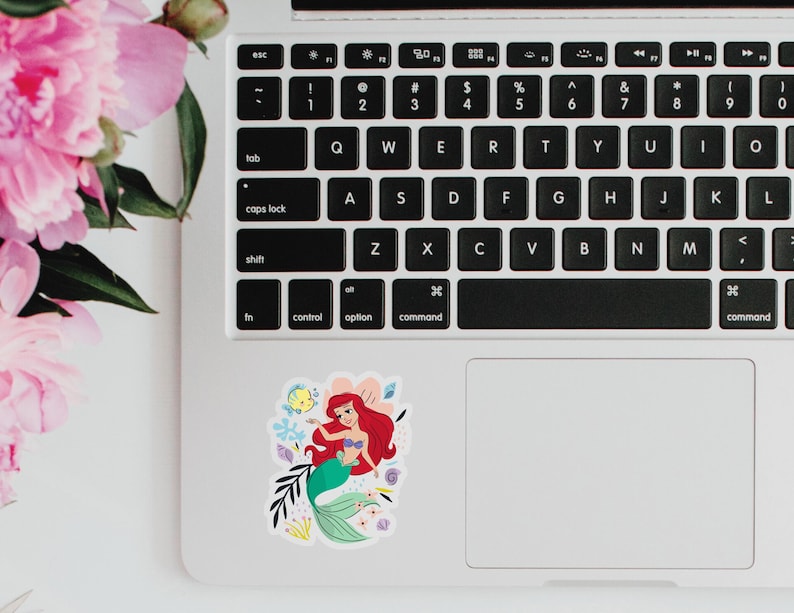 May include: A sticker featuring Ariel, the Little Mermaid, with her signature red hair and green tail. She is surrounded by colorful sea creatures and flowers.