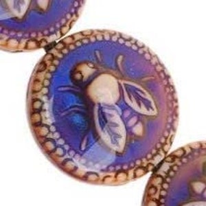 May include: Round, purple glass beads with a raised bee design. The bee is cream-colored with detailed wings. The beads have a decorative border of small, raised dots. The background is a gradient of purple and blue.
