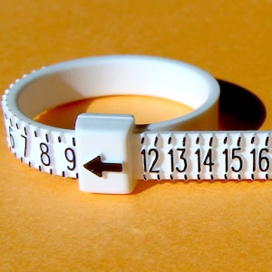 May include: White plastic ring sizer with black numbers from 6 to 17. The ring sizer has an arrow pointing to the right.