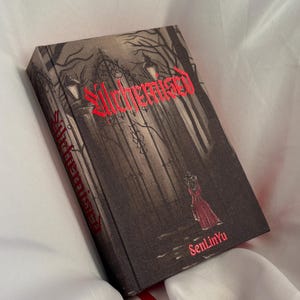 Può includere: Un libro con copertina rigida intitolato "Alchemised" con un'illustrazione gotica sulla copertina. La copertina presenta una scena scura e dettagliata con un cancello, alberi e una figura con un vestito rosso. Il titolo è in rosso e il nome dell'autore, SenLinYu, è visibile.