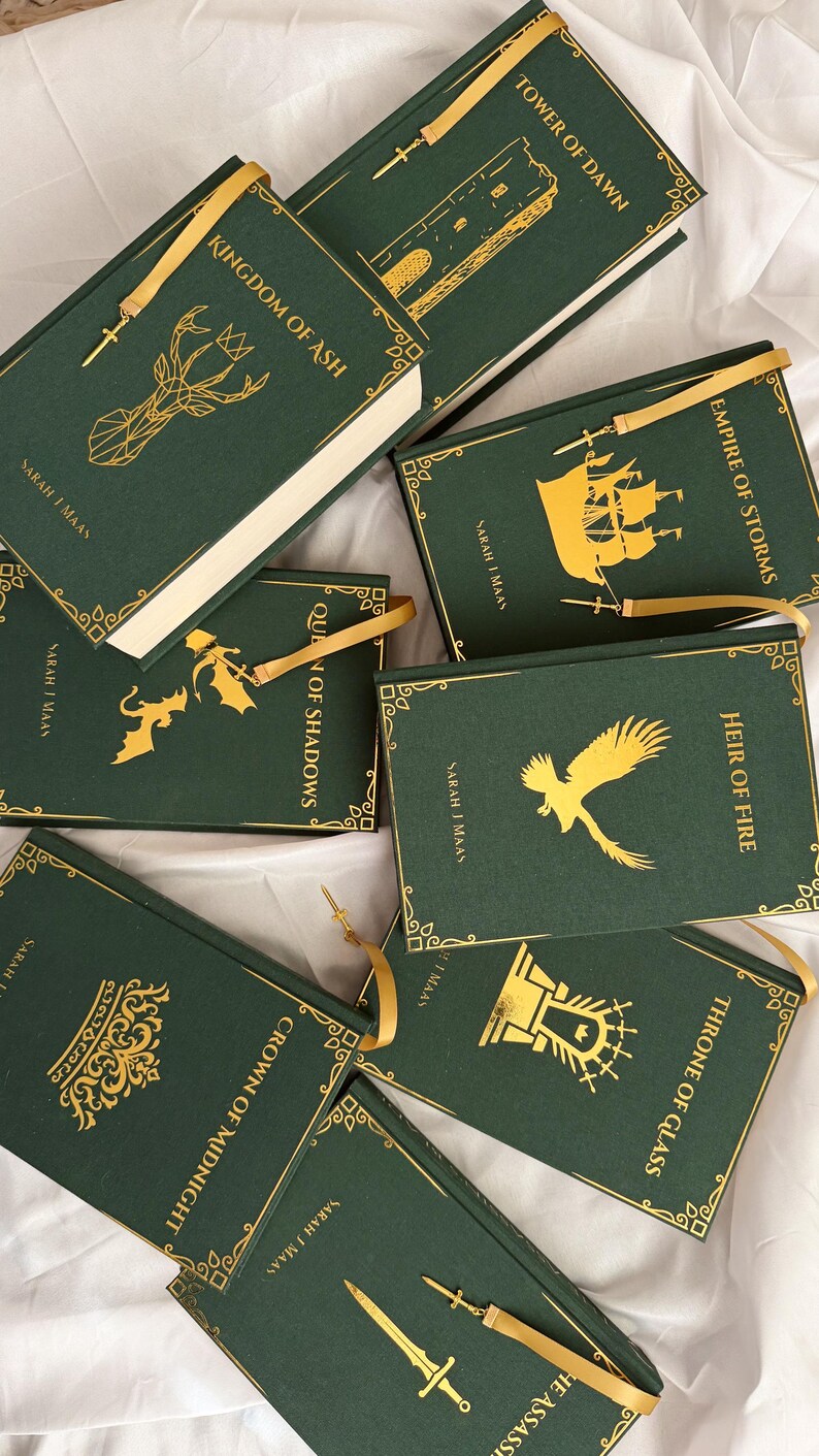 May include: A collection of eight dark green hardback books by Sarah J. Maas, each featuring gold foil illustrations and titles including Kingdom of Ash, Tower of Dawn, Empire of Storms, Queen of Shadows, Heir of Fire, Crown of Midnight, and Throne of Glass.