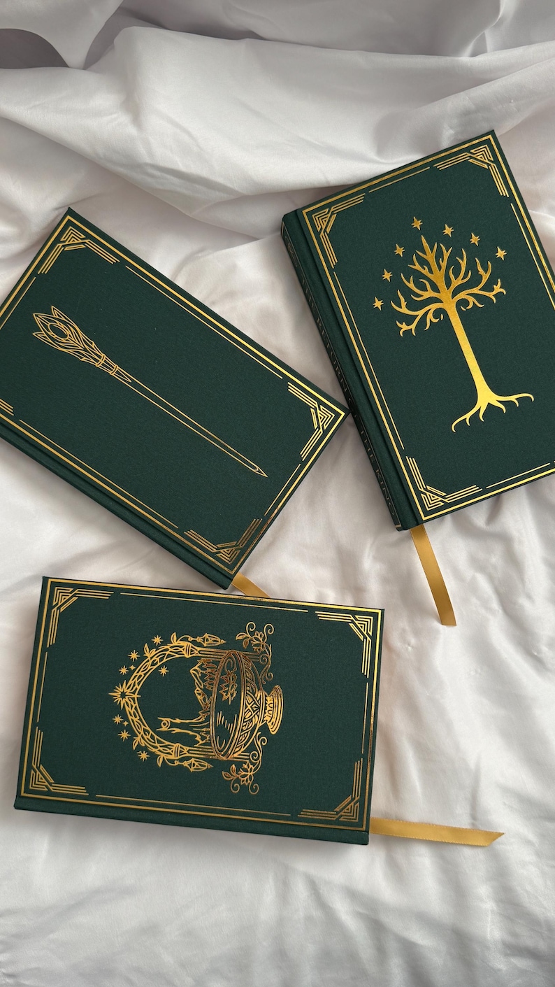 May include: Three dark green hardback books with gold foil detailing. One book features a gold tree and stars, another shows a staff, and the third displays a circular ornate emblem. Each book includes a gold ribbon bookmark and gold corner borders.
