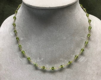 May include: A delicate gold chain necklace with small, round, green peridot beads.