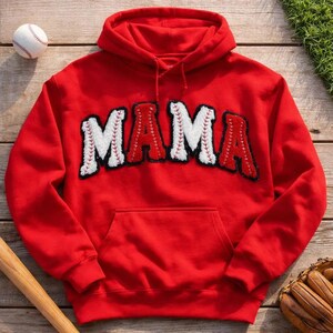 Könnte beinhalten: Ein leuchtend roter Kapuzenpullover mit dem Wort MAMA in großen, strukturierten Buchstaben. Die Buchstaben sind in einem weiß-roten Baseball-Design gestaltet und mit roten Nahtdetails versehen. Der Hoodie verfügt über eine Kängurutasche vorne.