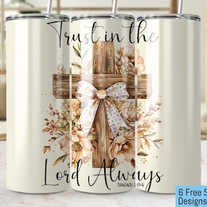 May include: A cream-colored tumbler with a floral cross design. The cross is made of wood and adorned with a bow and flowers. The text "Trust in the Lord Always" is written on the tumbler.