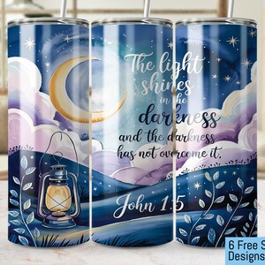 May include: A blue and purple watercolour tumbler with a crescent moon, stars, and a lantern. The tumbler has the text "The light shines in the darkness and the darkness has not overcome it. John 1.5" printed on it.