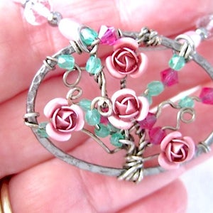 May include: A silver oval pendant with a wire-wrapped tree design featuring pink roses and green and red beads.