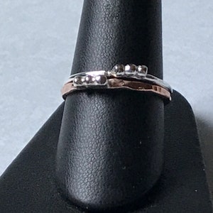 May include: Two thin silver rings with a row of small silver beads on the top ring. The bottom ring is a thin band of rose gold.