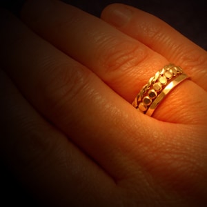 May include: A close-up of a hand wearing three gold rings. The rings are stacked on top of each other and have a textured design.