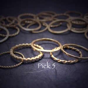 May include: A set of five gold rings, including a beaded ring, a twisted ring, and a plain band. The rings are stacked on top of each other and the text "Pick 5" is visible below the rings.