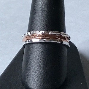 May include: A set of three silver and rose gold spinner rings. The rings are textured and have a hammered finish.