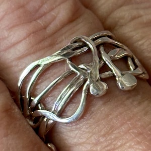 May include: A silver ring with a unique, abstract design. The ring is made of multiple intertwined bands that form a complex pattern.
