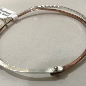 Puede incluir: Un brazalete de plata y cobre con un diseño texturizado. El brazalete está abierto y tiene un cierre con bisagra.