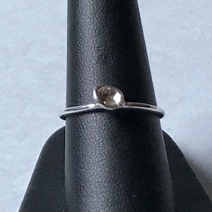 May include: A silver ring with a small, round, cup-shaped design on the top.