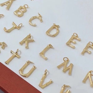 May include: A set of gold-coloured alphabet letter charms made of bamboo. The letters are arranged in alphabetical order, starting with A and ending with W.