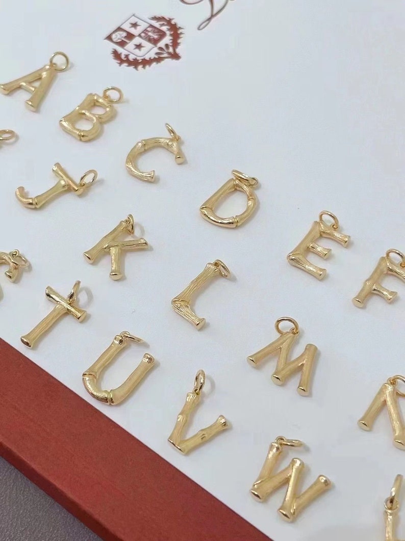 May include: A set of gold-coloured alphabet letter charms made of bamboo. The letters are arranged in alphabetical order, starting with A and ending with W.