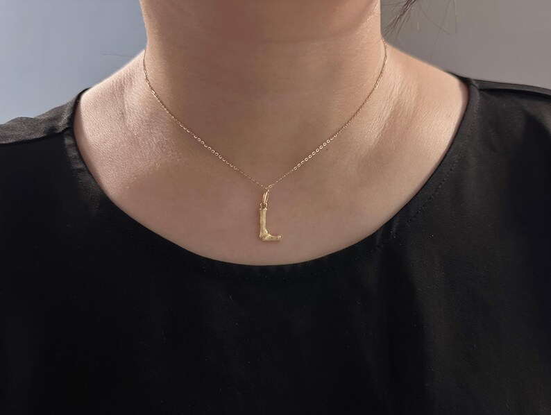 May include: A gold chain necklace with a small, abstract pendant in the shape of a leg.