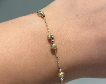 May include: A delicate gold bracelet with alternating gold and silver beads. The bracelet is on a person's wrist.