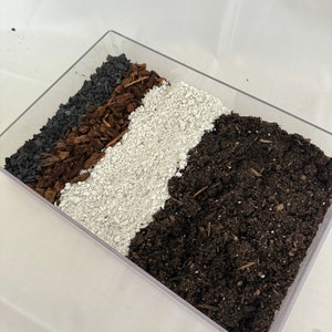 May include: A clear plastic tray filled with four layers of different potting mediums: black charcoal, brown wood chips, white perlite, and dark brown soil.