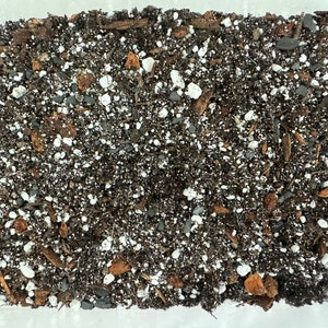May include: Close-up of a dark brown potting mix with white perlite, small pieces of bark, and other organic matter.