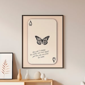 Pode incluir: Uma impressão emoldurada com uma borboleta preta e branca e o texto "You can't change the cards you were dealt just the way you play the hand".