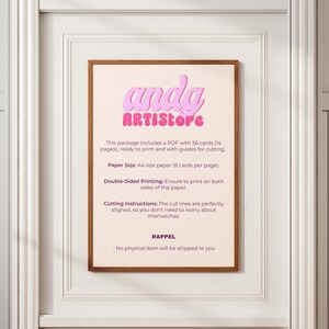 May include: A framed print with the text "anda ARTISstore" in pink bubble letters. The print includes instructions for printing cards, specifying A4 paper size and double-sided printing. The frame is brown, and the background is a light pink.