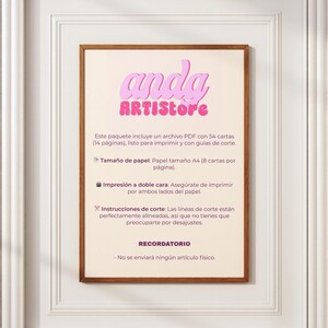 May include: A framed print with the text "anda ARTISTore" in pink, above Spanish text. The print is in a wooden frame and is hanging on a white wall. The text describes a PDF file with 54 cards, ready to print.