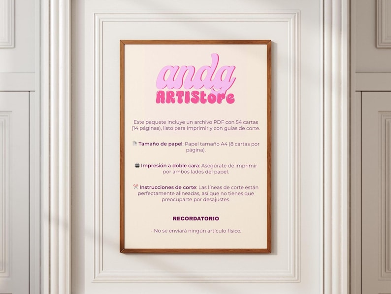 May include: A framed print with the text "anda ARTISTore" in pink, above Spanish text. The print is in a wooden frame and is hanging on a white wall. The text describes a PDF file with 54 cards, ready to print.