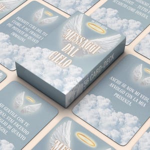 Puede incluir: Una baraja de 56 cartas titulada "Mensajes del Cielo" con ilustraciones de alas de ángel y halos. Las cartas y la caja presentan un fondo azul claro con imágenes de nubes y texto en italiano. La caja es rectangular y las cartas son cuadradas.