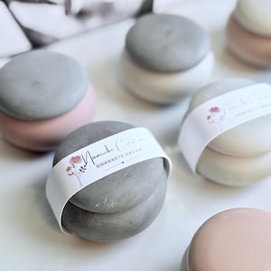 May include: Several small, round concrete decor items in shades of grey, pink, and white. Each has a matching lid and a white band with floral illustrations and the text "Namibe Creations CONCRETE DECOR". These items are suitable for home decor.