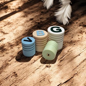 Könnte beinhalten: Vier farbige Holzkacheln mit den Buchstaben 'V', 'B', 'G' und einer weißen Feder auf einer Holzoberfläche.