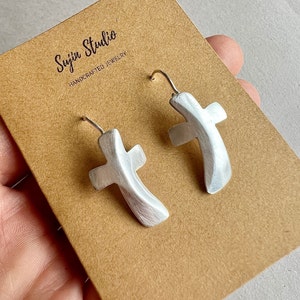 May include: Silver cross earrings with a textured finish. The earrings are on a brown card with the text "Suyin Studio Handcrafted Jewelry".