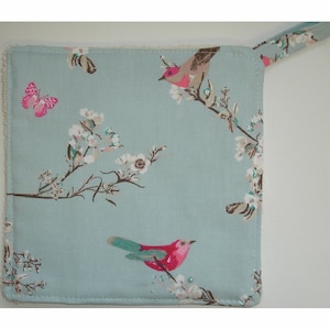 May include: A light blue kitchen towel with a floral pattern and two pink birds. The towel has a loop for hanging.