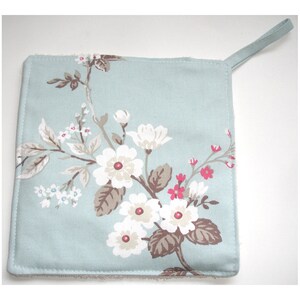 May include: A light blue pot holder with a floral pattern featuring white and pink flowers and brown leaves. The pot holder has a loop handle.