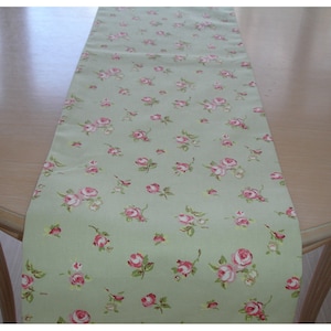 May include: A green table runner with a delicate floral pattern featuring small pink roses. The runner is made of a soft, smooth fabric and is perfect for adding a touch of elegance to any dining table.