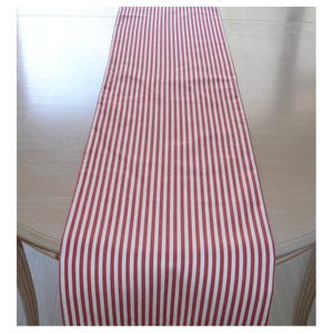 May include: Red and white striped table runner. The runner is made of a woven fabric and has a classic striped pattern.