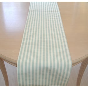 May include: A light blue and white striped table runner. The runner is made of a soft, woven fabric and has a subtle sheen.
