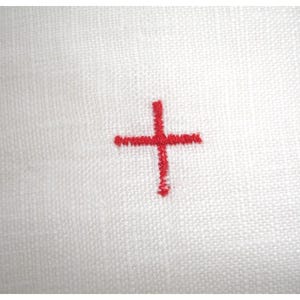 Peut inclure: Gros plan sur un tissu blanc avec une croix rouge brodée au centre. La croix est un motif simple à quatre bras, avec des coutures visibles. Le tissu a un aspect texturé.