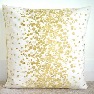 May include: White cushion with a gold embroidered design of scattered circles and ovals.