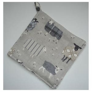 May include: A grey and white kitchen pot holder with a pattern of sheep wearing plaid and striped jumpers. The pot holder has a loop for hanging.