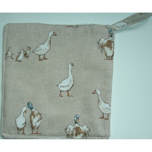 May include: A beige linen pot holder with a loop handle features a repeating pattern of white geese and brown ducks.