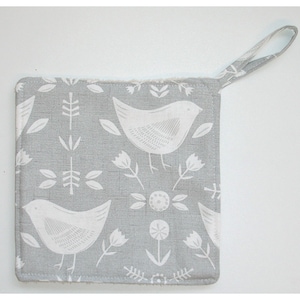 May include: A grey square potholder featuring a white bird and floral design. It has a hanging loop and a soft, textured edge. The pattern includes stylized birds, leaves, and flowers, perfect for kitchen use.