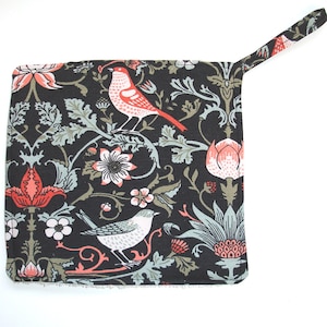 May include: A black fabric pot holder with a floral pattern featuring red and white flowers, green leaves, and two red and white birds. The pot holder has a loop handle.